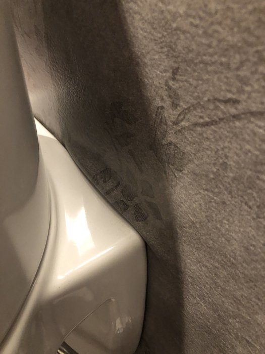 Vägghängd toalettstol med synliga märken på grå plastmatta vid golvanslutningen, tecken på möjligt installationproblem.
