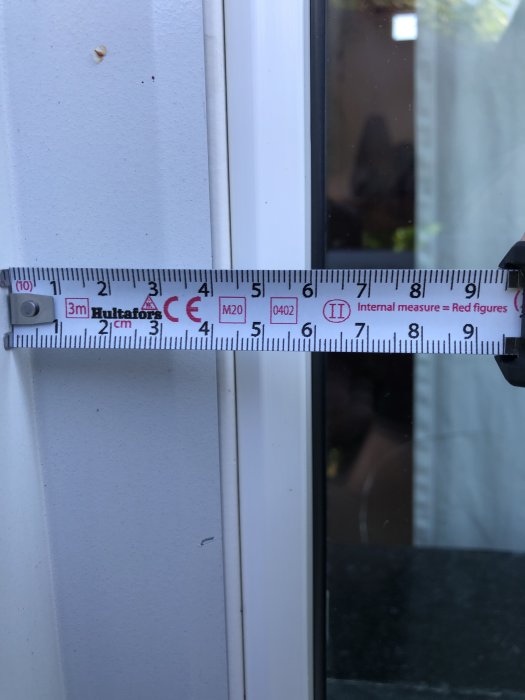 Måttband som visar avståndet mellan fönsterglas och karmkant på ett fönster.