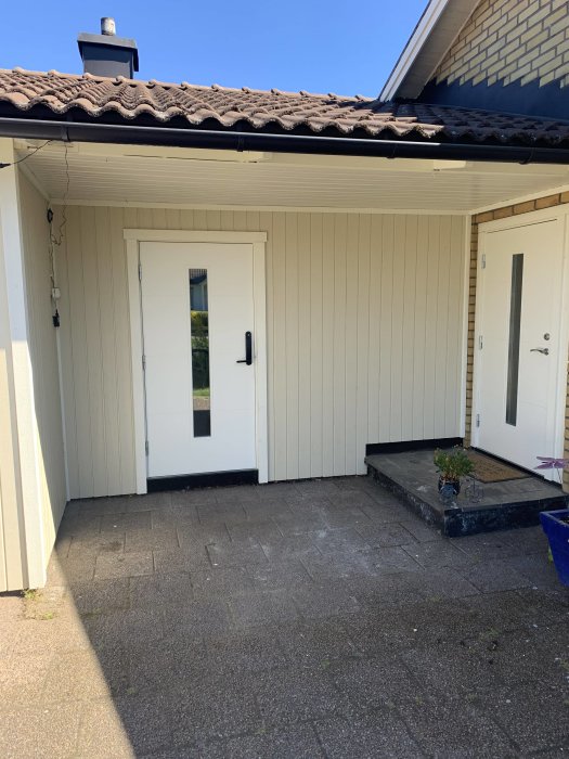 Ytterdörren till ett hus med en grovingång utan det nya trädäcket ännu på plats, stenplattor på marken.