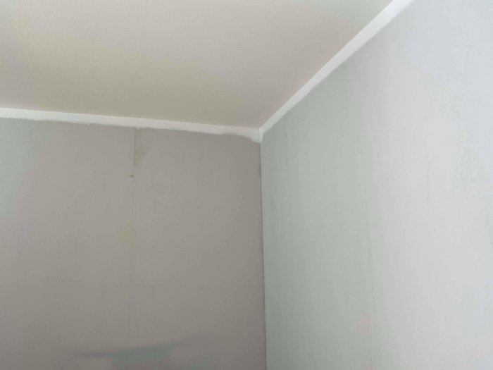 Hörn av ett rum under renovering med spacklade väggar och nymålat vitt tak.