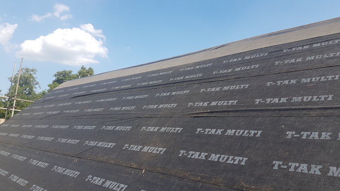 Nyuppfört hus med takpapp med veck och bulor, klar himmel i bakgrunden.