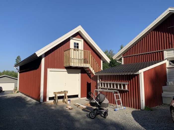 Rödmålat garage med nyinstallerad trappa till övre våning under blå himmel.