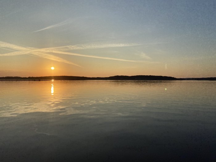 Solnedgång över stilla vatten med konturer av en ö i horisonten.