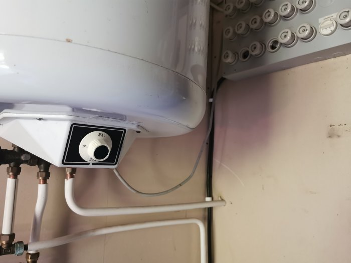 Värmepannas underdel med synlig rördragning och termostat mot en vägg med eldosor.