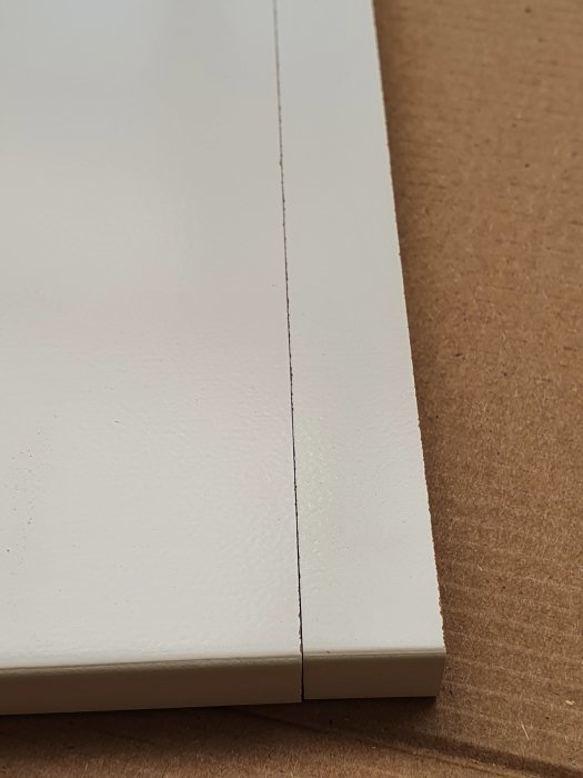 Närbild på ett sågat snitt i en vit laminattäcksida som inte är helt frasfri.