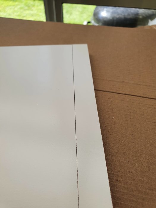 Närbild av ett sågat snitt i vit laminatskiva ovanpå brun kartong.