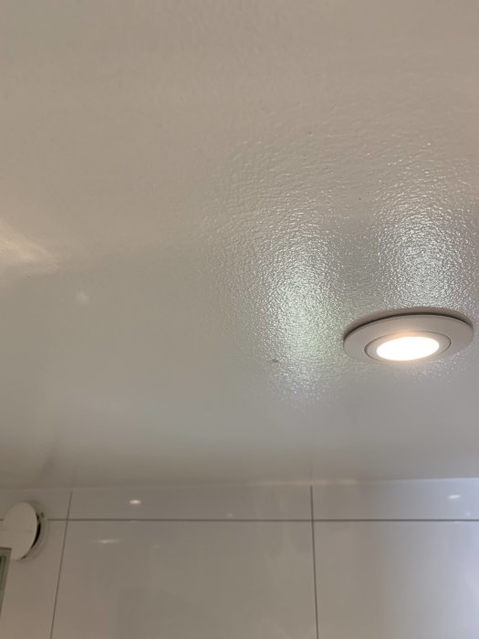 Glansigt tak med våtrumsmembran och inbyggd spotlight i ett badrum.