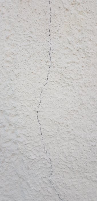 En närbild av en husfasad med grov puts och en lodrät spricka, symbol för potentiella sättningsskador.