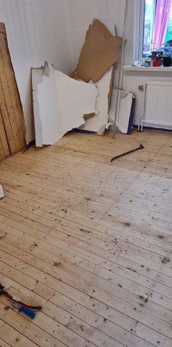 Ett delvis rivet golv i ett rum, synliga spånskivor och byggavfall vid väggen.