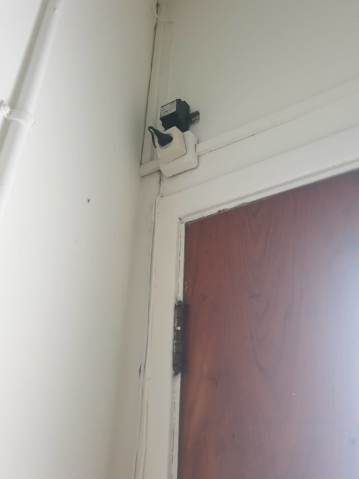 Gammal dörröppnare och intercom installerade över en träförsedd dörr.
