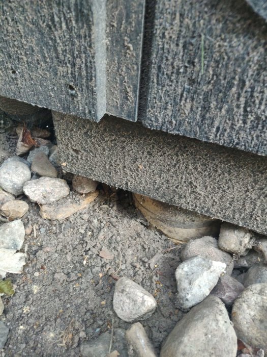 Närbild på en byggplint och en träregelns utsida med småstenar runtomkring.