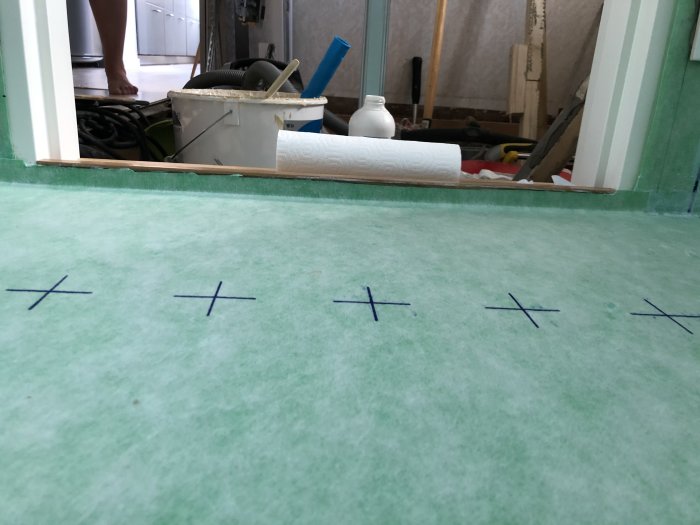 Nyinstallerat tätskikt på badrumsgolv med synliga markeringar och renoveringsverktyg i bakgrunden.