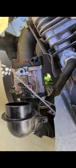 Närbild av en motors komponent med markerad del, troligen ett förgasarproblem eller underhåll.