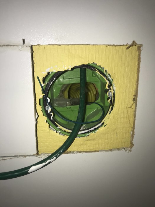 Öppnat eluttag i vägg med grön kabel och gult rör, osäkerhet om kablage för fiberanslutning.