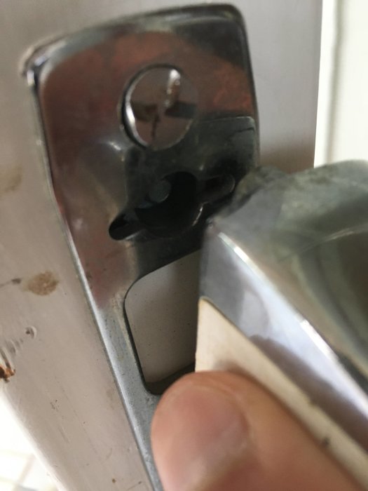 Närbild på en dörrhandtagsmekanism med synlig skada runt låskolven.