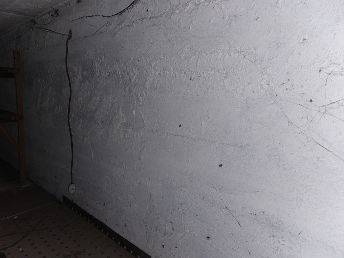 Blottad betongvägg under trappa med synliga kablar och utan cementputs.
