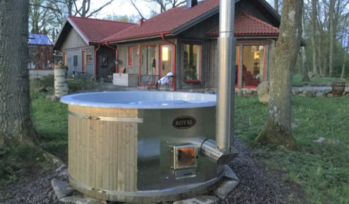 Vedeldad badtunna för 6 personer, med plast invändigt, installerad utomhus nära ett rött hus.