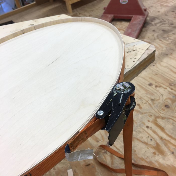 Oval träbricka med kant laminerad med björkplywood, fäst med metallspännare på arbetsbänk.