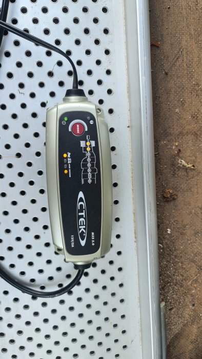 Batteriladdare från CTEK ansluten och igång, placerad på en metallhylla.