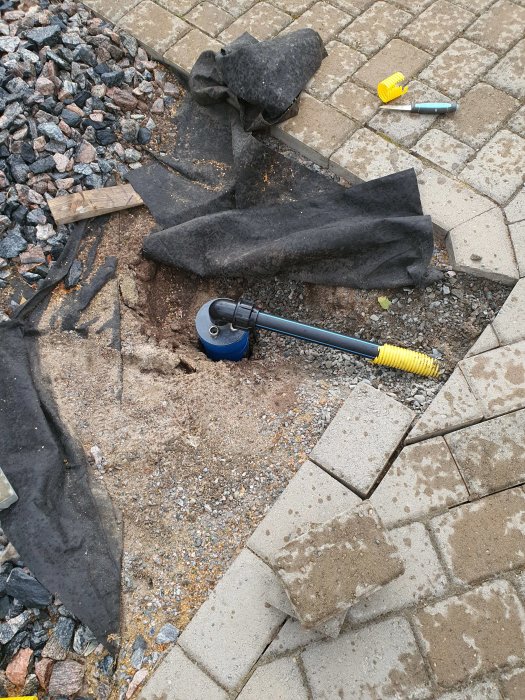 Nyligen installerat brunnslock och PVC-rör i grävd brunn med verktyg på stenläggning.