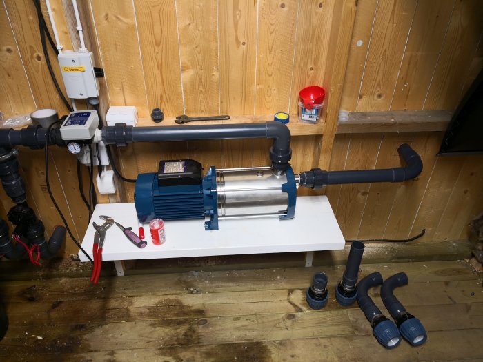 Bevattningssystem med Plurijet pump och tryckkontroll installerat på en hylla, omgiven av verktyg och omonterade rör.