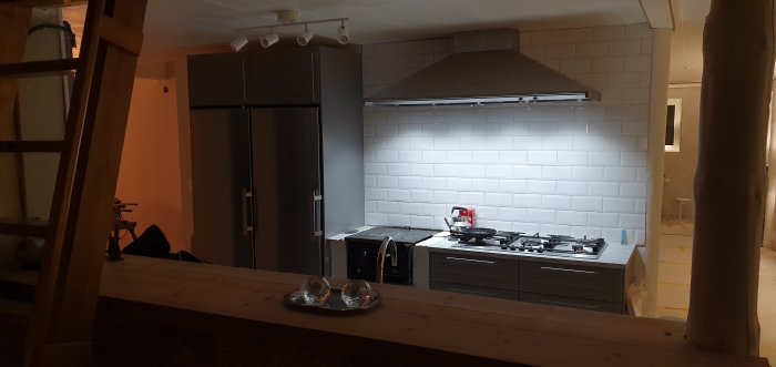 Renoverat kök med vit kakelvägg, rostfria vitvaror och spis samt tecken på pågående byggnation.