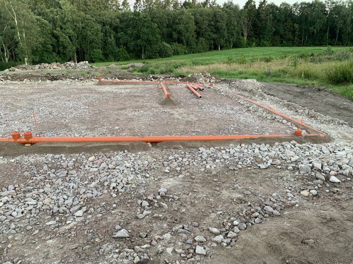 Markarbete för dagvatten med orangea rör och grus 0-8 runt om på en byggplats omgiven av grönska.