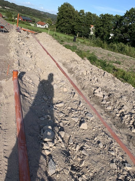 Grus och stenar runt ett dagvattenrör på en byggarbetsplats med skugga av fotografen.