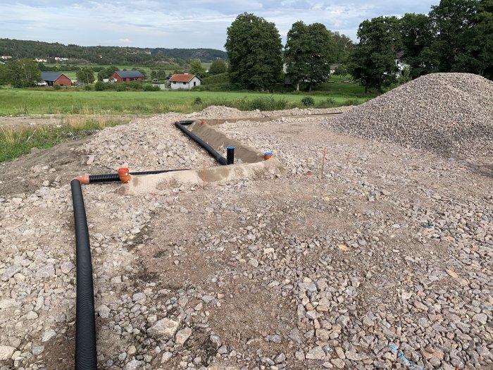 Arbetsplats för dagvatten med rör och grus, grushög i bakgrunden på byggprojekt.