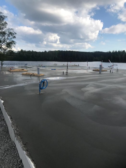 Nyutgjuten betongplatta med härdande yta, uppställda verktyg, mot en bakgrund av träd och en sjö.