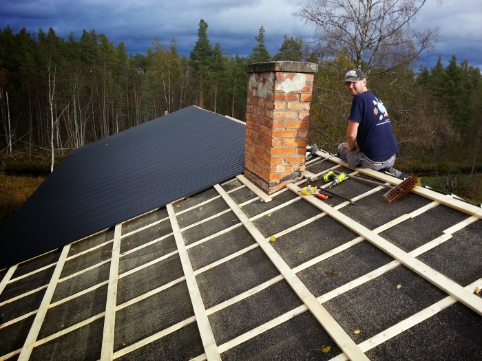 Renovering av plåttak på sommarstuga med person som arbetar, verktyg och skog i bakgrunden.