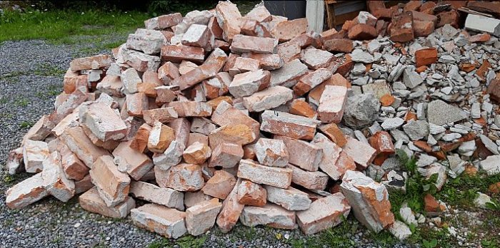 En hög med lösa, använda tegelstenar i olika storlekar och färger, några med murbruk, på en grusig mark.