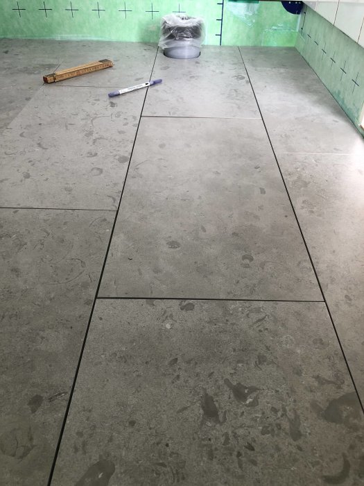 Oskarpa granitkeramikplattor som är kapade och utlagda på ett golv, med verktyg och en brunnskant synliga.