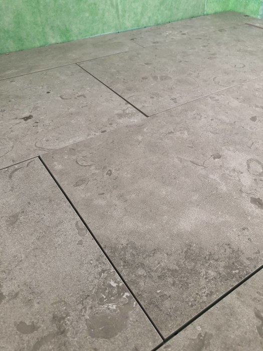 Kapade granitkeramikplattor på golv nära brunnen, redo för sättning med lätta flisor synliga.