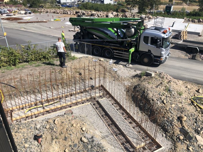 Armeringsjärn uppställda för betonggjutning med betongbil och arbetare i bakgrunden.