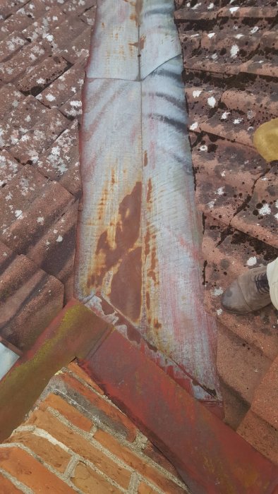 Rostig plåt på tak med tegelpannor och ränndal synlig vid ett renoveringsprojekt.