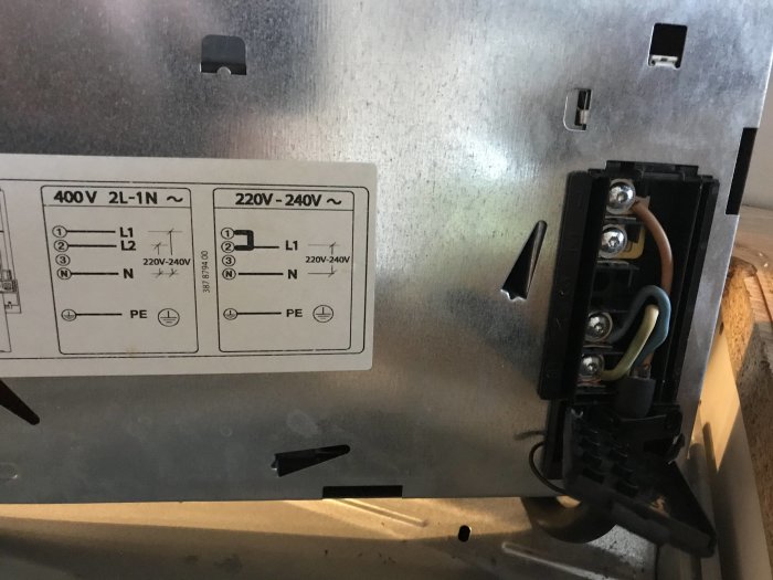 Anslutningsplint på baksidan av en spishäll med kablar kopplade, etikett med elektrisk information synlig.