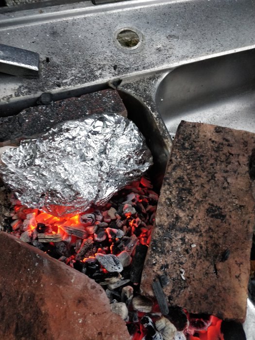 Kyckling inlindad i folie som ligger på glödande kol i en grill.