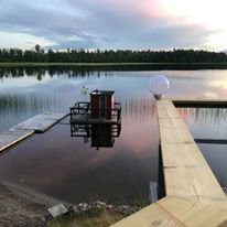 Ett litet hus på en brygga som sträcker sig ut i en spegelblank sjö vid skymningen.