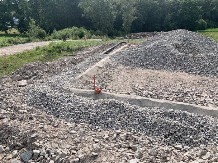 Nyjusterad dräneringsdike fylld med makadam, omgiven av sten och grus på en byggplats.