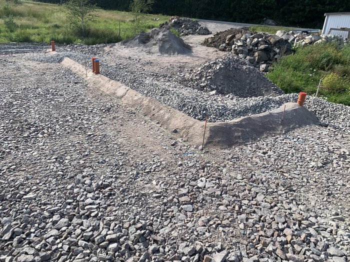 Grundarbetsområde med utstickande rörbitar för dagvattenanslutningar, grushög och sand.