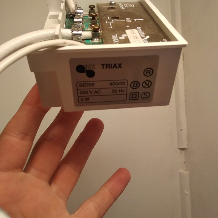 Hand håller ett öppet Triax elektronikhölje med synliga kretsar och etiketter.