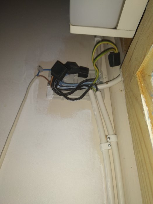 En oorganiserad samling av elektriska kablar och kopplingar i ett hörn nära ett fönster.