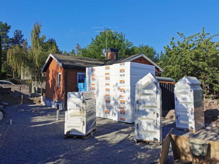 Nya isolerade grundelement levererade och omslutna av skyddsplast står framför en liten byggnad på en byggarbetsplats.