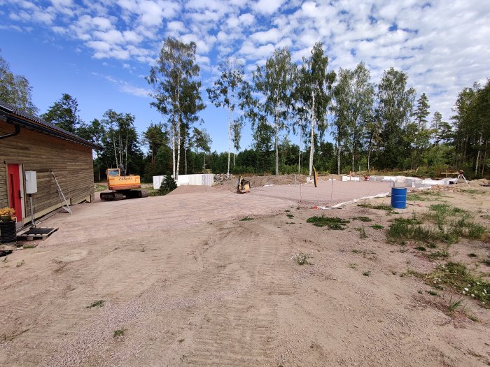 En byggarbetsplats med förberedd mark för grunden, kantelement i bakgrunden och grävmaskin.