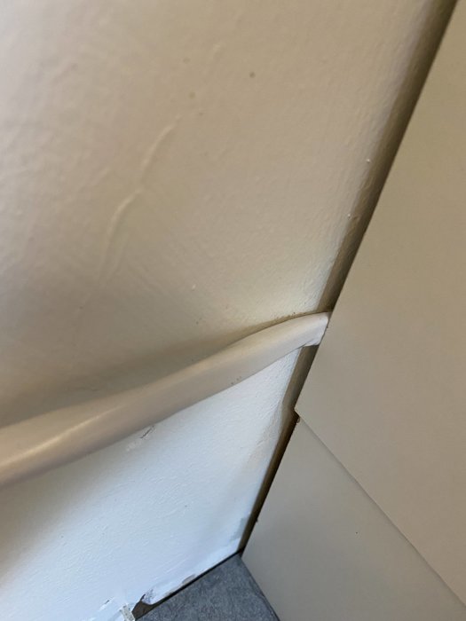 Elkabel i kläm bakom underskåpets golvsockel i kök, utan yttre isolering eller skydd.