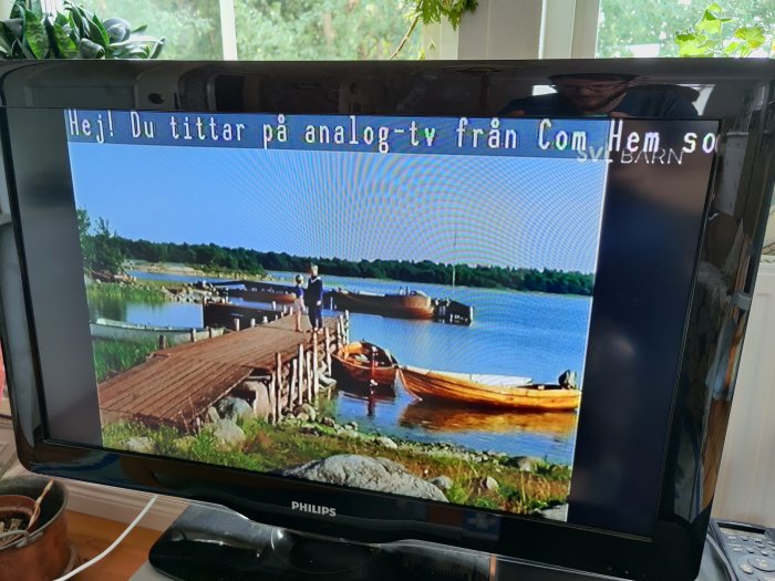 Analog-TV-skärm som visar en sommarbild med brygga, båt och skog. Text på skärmen "Hej! Du tittar på analog-tv".