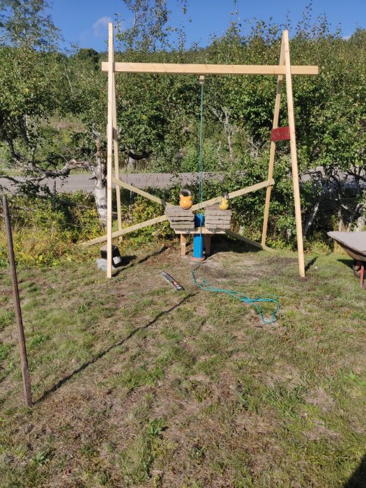 En enkel träställning med pluncher och ett foderrör för brunnsborrning i en trädgård.