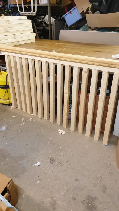 Träräcke under konstruktion, med vertikala baluster och överliggare, i ett rörigt garage.