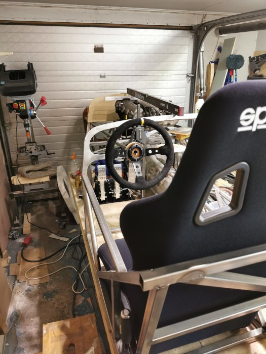 Verkstadsmiljö med en racingsimulatoruppbyggnad i metall och en svart racingstol.